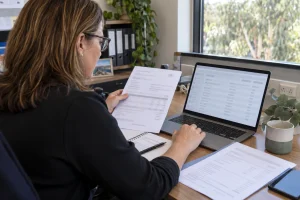 Australian small-business owner checking company registration details on a laptop against business documents
